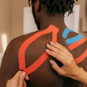 Close up of kinesio tape application on a man's shoulder for pain relief therapy.