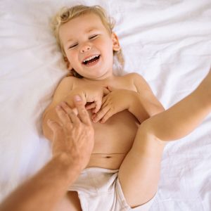 A happy child laughing while being tickled in a playful moment on a white bed.