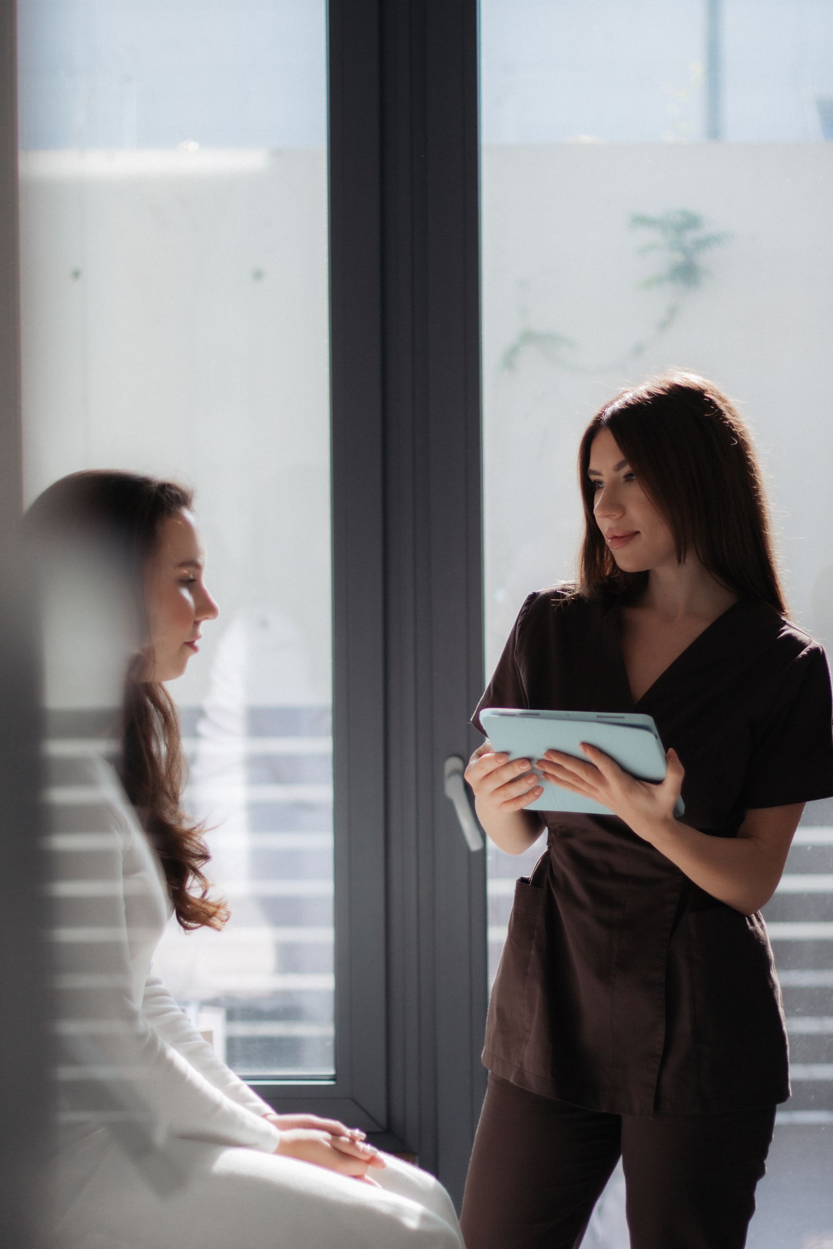 Two women in a modern office setting engaged in a consultation, using a tablet.